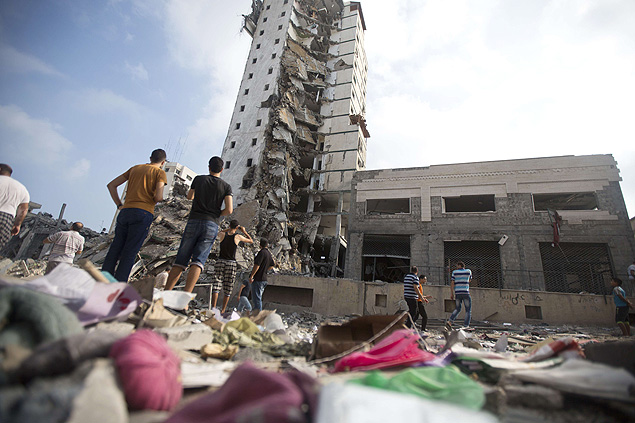 Palestinos olham prédio destruído (Folhapress)